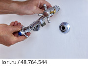 Hands are removing used two handle faucet from wall fitting, worn metal fixture with cross handles and missing spout is separated from exposed connector. Стоковое фото, фотограф Владимир Григорьев / Фотобанк Лори