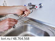Using adjustable wrench plumber tightens mounting nut of spout on dual handle wall mounted faucet with hidden pipework inside wall. Стоковое фото, фотограф Владимир Григорьев / Фотобанк Лори