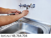 Man is replacing wall-mounted faucet spout using hands without tools while water traces remain near sink on metal countertop. Стоковое фото, фотограф Владимир Григорьев / Фотобанк Лори