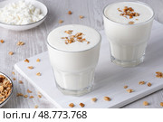 Kefir, buttermilk or yogurt, cottage cheese with granola. Yogurt in glass on white wooden background. Probiotic cold fermented dairy drink. Gut health, fermented products, healthy gut flora concept. Стоковое фото, фотограф Наталия Попова / Фотобанк Лори