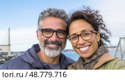 A snapshot of middle age mixed race couple smiling outdoors. Стоковое AI-изображение, AI-художник Анастасия Золотницкая / Фотобанк Лори