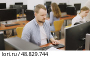 Side view on concentrated male student sitting at library desk with pc, preparing for exam in computer class. Стоковое видео, видеограф Яков Филимонов / Фотобанк Лори