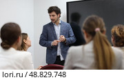 Young male teacher near interactive board, gesturing with hand while consecrating topic of lesson for adults in classroom. Стоковое видео, видеограф Яков Филимонов / Фотобанк Лори