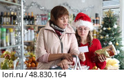 Family of mother and daughter with cart shopping at supermarket, looking for something and reviewing and checking list of products to buy. Christmas shopping. Стоковое видео, видеограф Яков Филимонов / Фотобанк Лори