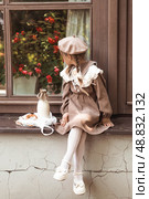 Vintage accessories and retro-style clothes. A small, beautiful girl with bows in her hair, in a beige dress and a beret outdoors with bagels and milk in a string bag. Стоковое фото, фотограф Photojuli / Фотобанк Лори