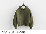 Blank khaki green hoodie sweatshirt long sleeve hanging on simple hook against a white wall. Hoody with hood. Design, print mockup. Template sport clothes. Front view. Gender neutral. Brand, logo. Стоковое AI-изображение, AI-художник Марина Демидюк / Фотобанк Лори