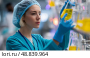 Laboratory technician conducting research with yellow liquid samples in a modern lab environment. Стоковое AI-изображение, AI-художник Сергей Толмачёв / Фотобанк Лори