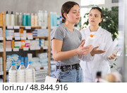Young woman choosing cream while pharmacist offering in drugstore. Стоковое фото, фотограф Яков Филимонов / Фотобанк Лори