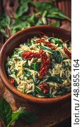 Creamy Orzo Pasta With Spinach and Sun-Dried Tomatoes in a Rustic Bowl Surrounded by Fresh Greenery. Стоковое AI-изображение, AI-художник Юлия Гапеенко / Фотобанк Лори
