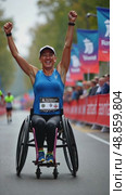 A woman in a wheelchair raises her right arm in a fist pump as she crosses the finish line of a marathon. The background is filled with spectators cheering the winner. Parasports competitions. Стоковое AI-видео, аниматор Sergey Grishin / Фотобанк Лори