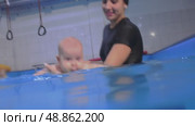Baby swimming with instructor in indoor pool. Стоковое видео, видеограф Константин Шишкин / Фотобанк Лори