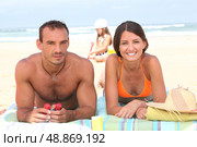 Parents sunbathing as their daughter plays in the sand behind them. Стоковое фото, агентство Ingram Publishing / Фотобанк Лори