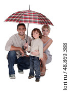 Young family sheltering under an umbrella. Стоковое фото, агентство Ingram Publishing / Фотобанк Лори