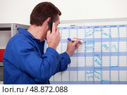 Man in blue overalls talking on the phone and writing on a board. Стоковое фото, агентство Ingram Publishing / Фотобанк Лори