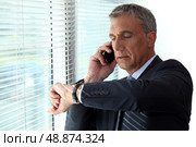 Businessman checking time whist on telephone call. Стоковое фото, агентство Ingram Publishing / Фотобанк Лори