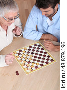 Senior woman playing checkers with a young man. Стоковое фото, агентство Ingram Publishing / Фотобанк Лори