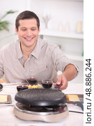 Man enjoying raclette at home with friends. Стоковое фото, агентство Ingram Publishing / Фотобанк Лори