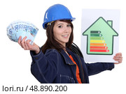 Tradeswoman holding up an energy efficiency rating chart and a wad of money. Стоковое фото, агентство Ingram Publishing / Фотобанк Лори