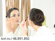 Brunette applying mascara in mirror. Стоковое фото, агентство Ingram Publishing / Фотобанк Лори