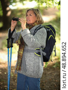 60 years old blonde woman is contemplating landscapes with binoculars, she’s wearing warm clothes and using a crook. Стоковое фото, агентство Ingram Publishing / Фотобанк Лори