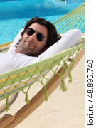 Man laid in hammock by swimming pool. Стоковое фото, агентство Ingram Publishing / Фотобанк Лори