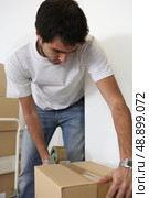 Young man taping shut a cardboard box. Стоковое фото, агентство Ingram Publishing / Фотобанк Лори