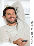 Man watching television in a white room using a remote control. Стоковое фото, агентство Ingram Publishing / Фотобанк Лори
