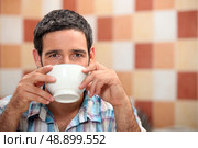 Man drinking from a white bowl in a tiled kitchen. Стоковое фото, агентство Ingram Publishing / Фотобанк Лори