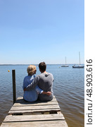 Couple sitting on the end of a pontoon with their arms around each other. Стоковое фото, агентство Ingram Publishing / Фотобанк Лори