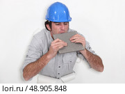 Fed-up tradesman biting a tile. Стоковое фото, агентство Ingram Publishing / Фотобанк Лори