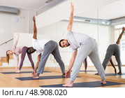 Young bearded man standing in twisting asana Parivrtta Prasarita Padottanasana. Стоковое фото, фотограф Яков Филимонов / Фотобанк Лори