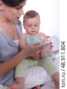 Mother resting baby on knee whilst looking at mobile telephone. Стоковое фото, агентство Ingram Publishing / Фотобанк Лори