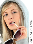 Woman in a hooded sweatshirt biting her sunglasses. Стоковое фото, агентство Ingram Publishing / Фотобанк Лори