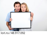 Couple pulling a funny face and holding a blank board ready for your text. Стоковое фото, агентство Ingram Publishing / Фотобанк Лори