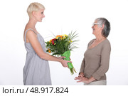 Young woman offering a bouquet of flowers to her grandmother. Стоковое фото, агентство Ingram Publishing / Фотобанк Лори