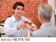 Young man and senior chinking wine glasses. Стоковое фото, агентство Ingram Publishing / Фотобанк Лори