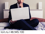 Businessman sitting on a bed in hotel room with laptop. Стоковое фото, агентство Ingram Publishing / Фотобанк Лори