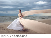 Fashionable model with extremely long dress like a wings. Vogue style. Beautiful model walks at the beach. Стоковое фото, агентство Ingram Publishing / Фотобанк Лори