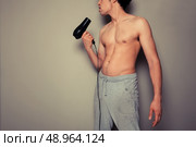 Athletic young man is holding a hair dryer and messing around with it. Стоковое фото, агентство Ingram Publishing / Фотобанк Лори