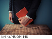 Man standing behind a desk with a red book in his hand. Стоковое фото, агентство Ingram Publishing / Фотобанк Лори