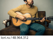 Young man playing guitar on sofa. Стоковое фото, агентство Ingram Publishing / Фотобанк Лори