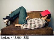 Man on sofa with book on his face. Стоковое фото, агентство Ingram Publishing / Фотобанк Лори