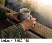 A young persons hands holding a mug with a hot beverage by a pond in a park at sunset in the winter. Стоковое фото, агентство Ingram Publishing / Фотобанк Лори