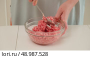 A person is mixing raw minced meat using a spoon in a clear glass bowl during home meal preparation or cooking. Стоковое видео, видеограф Андрей Журавлев / Фотобанк Лори