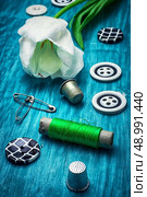white tulip and buttons for clothing on light blue wooden background.the image is tinted in vintage style. thread and buttons. Стоковое фото, агентство Ingram Publishing / Фотобанк Лори