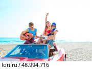young group having fun on the beach playing guitar and dancing in a convertible car. Стоковое фото, агентство Ingram Publishing / Фотобанк Лори