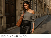 Стильная девушка в сером свитере и кожаной юбке прогуливается по старинной улице европейского города после дождя. Стоковое AI-изображение, AI-художник Оксана Хорватич / Фотобанк Лори