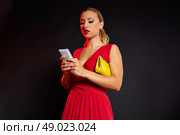 Blond fashion woman writing smartphone on black background and red dress. Стоковое фото, агентство Ingram Publishing / Фотобанк Лори