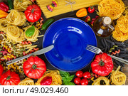 Raw pasta with ingridients and blue plate. Raw pasta with ingridients and copy space on empty blue plate with steel fork and knife. Стоковое фото, агентство Ingram Publishing / Фотобанк Лори