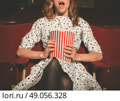 A young woman is sitting on the front row in a movie theater and is watching an exciting film while eating popcorn. Стоковое фото, агентство Ingram Publishing / Фотобанк Лори
